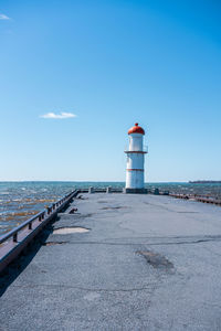 Lighthouse by sea against clear blue sky