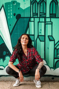 Portrait of a smiling young woman sitting against wall