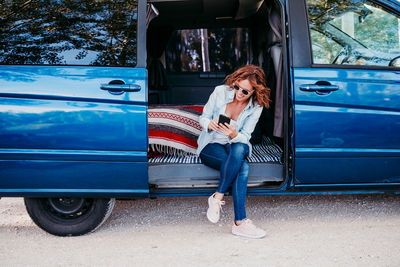 Woman wearing sunglasses using mobile phone in camper trailer