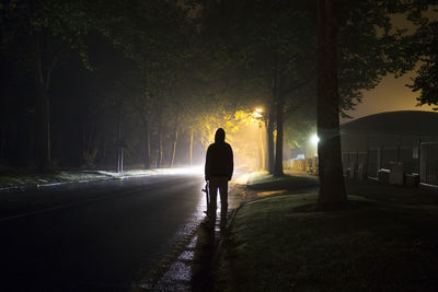 Rear view of skateboarder standing on road at night