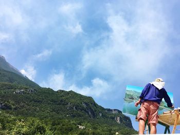 Rear view of woman standing on mountain against sky