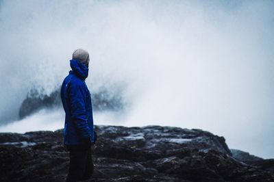 Rear view of man standing on rock against sky