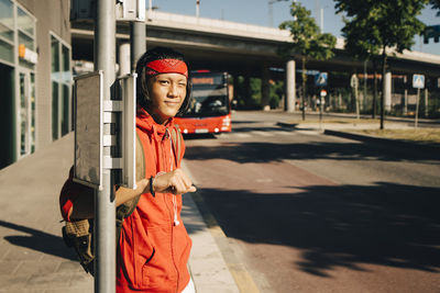 Portrait of smiling young man winking while standing at bus stop during sunny day