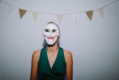 Portrait of woman wearing mask standing against wall