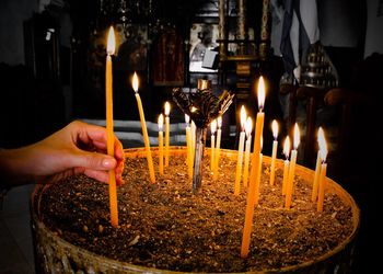 Cropped hand of woman placing lit candle in container at church