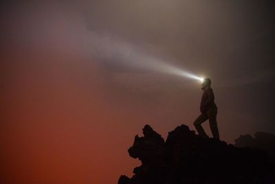 Woman with head torch standing against orange sky