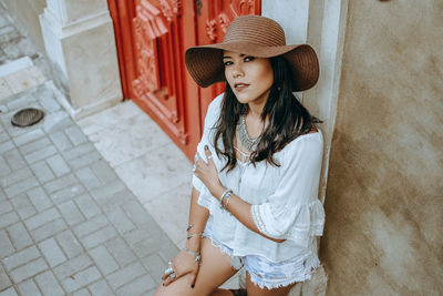 Young woman wearing hat standing against wall