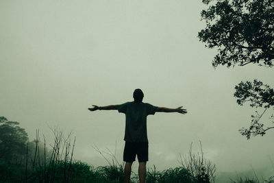 Rear view of man with arms outstretched standing against sky