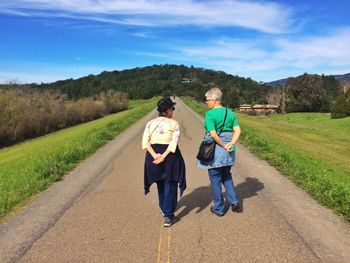 Rear view of man walking on road in field