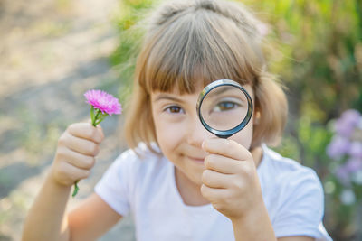 Portrait of girl holding flower looking through magnifying glass