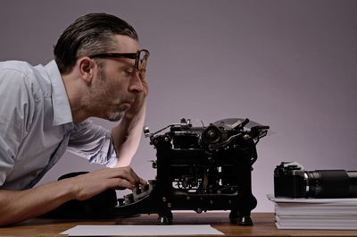 Side view of mature man using typewriter on table against wall at office