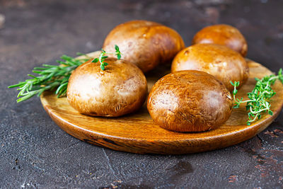 Fresh delicious portobello mushrooms with thyme and rosemary on wooden cutting board.