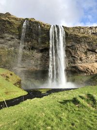 Scenic view of landscape with waterfall against sky