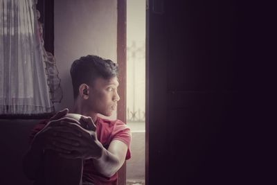 Thoughtful teenage boy looking though door at home