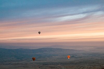 Hot air balloons flying over landscape against sky during sunset