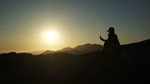 Silhouette man sitting on mountain against sky during sunset