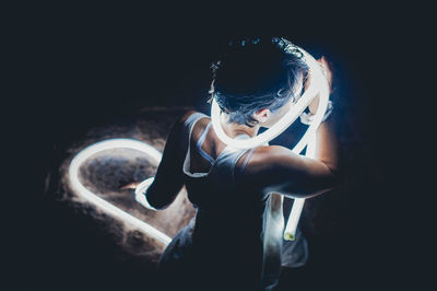 Rear view of mid adult woman holding illuminated fiber optic cable in darkroom