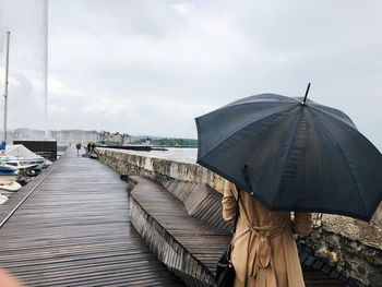 Rear view of woman holding umbrella while standing on pier against sea