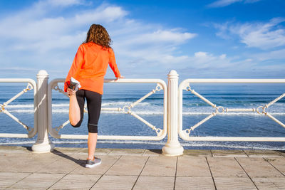 Rear view of woman standing on railing against sea