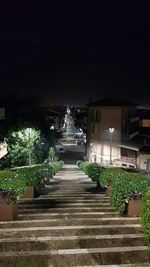 Illuminated footpath amidst buildings against sky at night