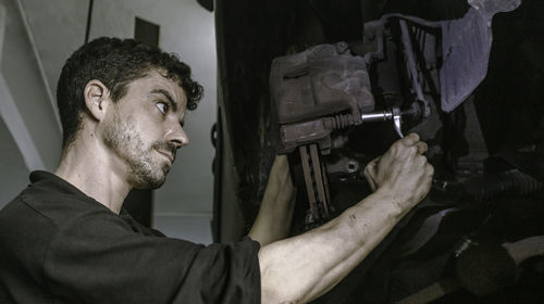 Low angle mechanic using ratchet to adjust car brake disc detail while working in garage