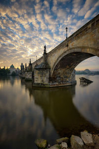 Arch bridge over river by buildings against sky