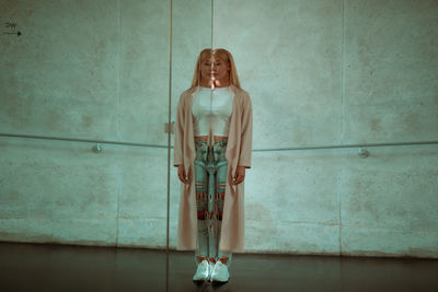 Young woman standing by mirror with reflection against wall