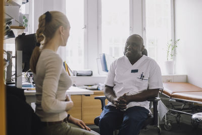 Smiling male healthcare worker discussing with female patient during visit in clinic