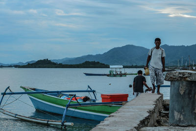 Rear view of man sitting on boat on lake against sky