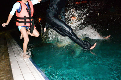 Friends jumping in swimming pool at night