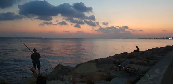 Man fishing in sea against sky during sunset