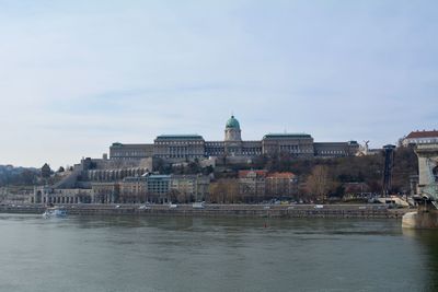 Buildings at waterfront against cloudy sky