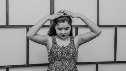 Girl with hand in hair standing against wall at home