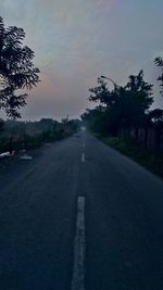 Road by trees against sky during sunset