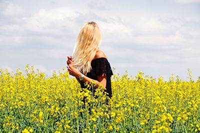 Young woman with hand in hair standing on oilseed rape field