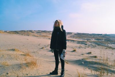 Full length of thoughtful woman standing on sandy landscape against sky