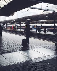 Person standing with suitcase at railroad station platform