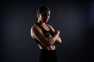 Side view of young woman standing against black background