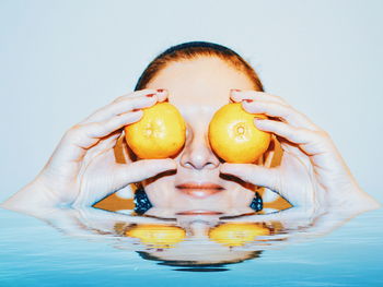 Woman covering eyes with fruits in bathtub