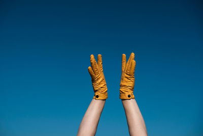 Cropped hands of woman wearing gloves against blue sky