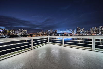 Illuminated bridge by buildings against sky at night