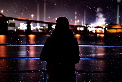 Rear view of silhouette woman standing on wet illuminated street at night