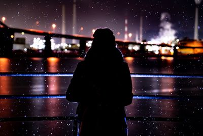 Rear view of silhouette woman standing in illuminated city during snowfall