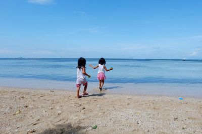 Rear view of sisters playing at beach against blue sky