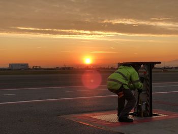 Side view of man standing on road against sky during sunset