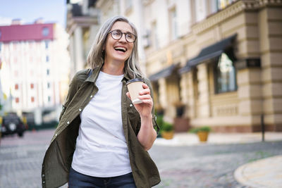Stylish senior woman with grey hair holding coffee cup while enjoying vibrant atmosphere of europe. 
