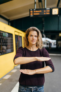 Portrait of woman gesturing equal sign while standing at railroad station platform