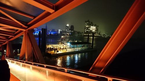Illuminated bridge over river by buildings against sky at night