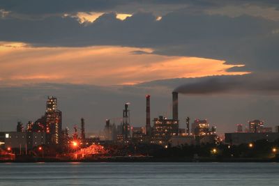 Illuminated factory against sky at sunset