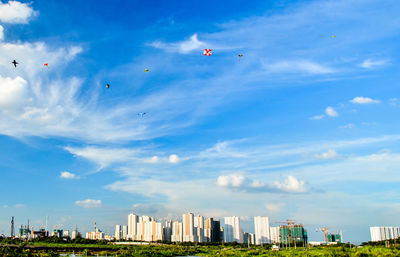 Low angle view of kites flying in blue sky over city